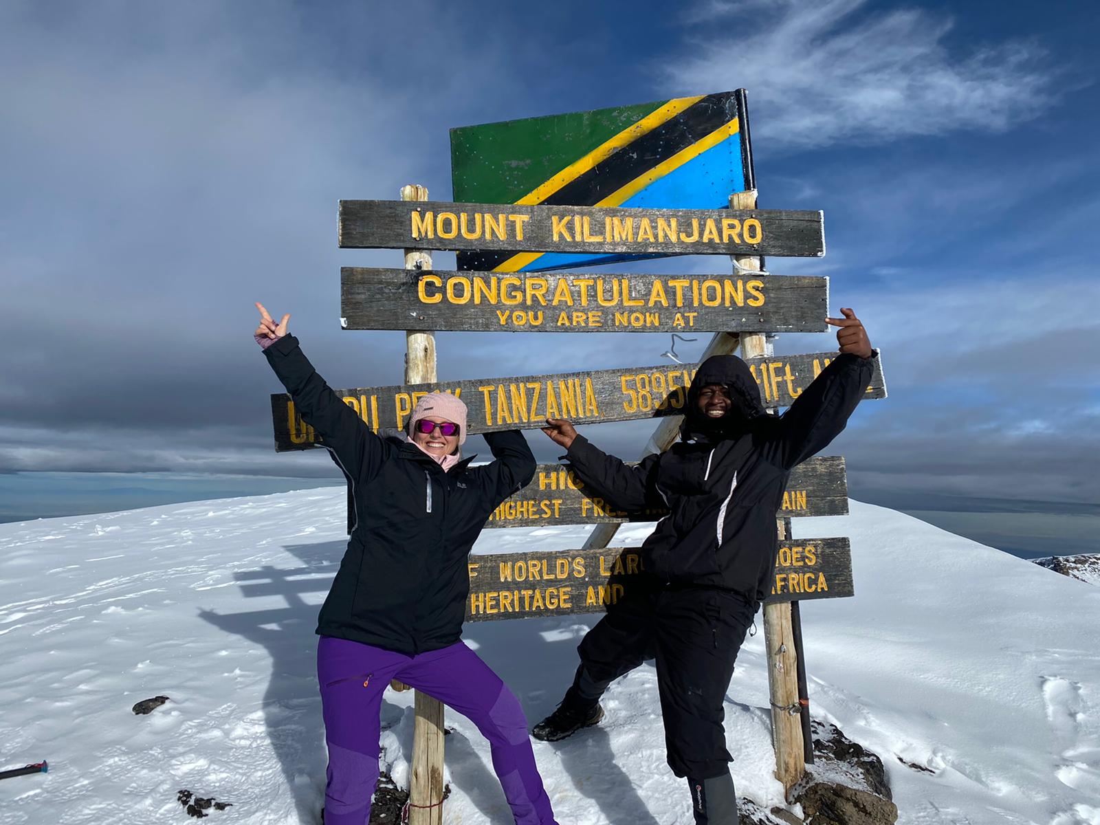 tourist and a guide at the summit of kilimanjaro